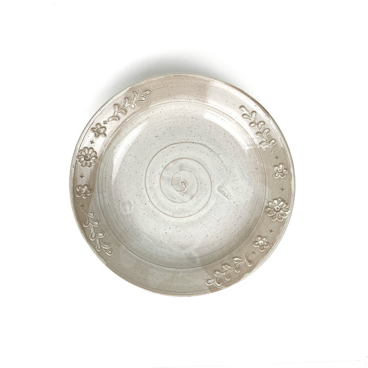 Overhead view of a speckled, glazed ceramic plate with a spiral center and embossed floral and leaf border.