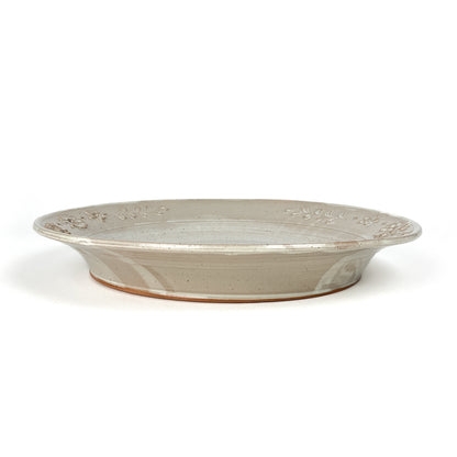 Side view of a shallow, speckled, glazed ceramic dish with an embossed floral and leaf design around the rim.