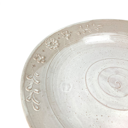 Close-up of a speckled, glazed ceramic plate showing the spiral center and embossed floral and leaf details on the rim.