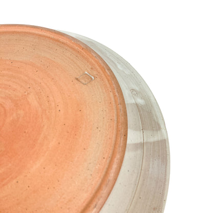 Close-up of the textured, unglazed base of a speckled ceramic plate with a faint maker's mark.