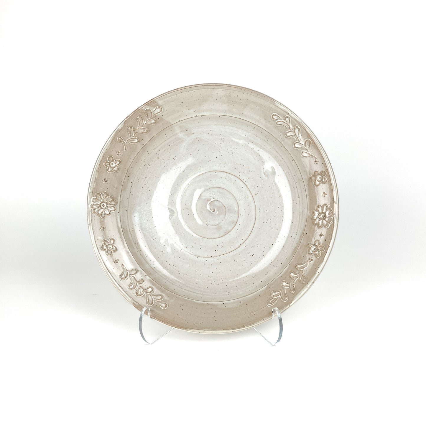 Speckled, glazed ceramic plate with a spiral center and embossed floral border, displayed on clear stands.