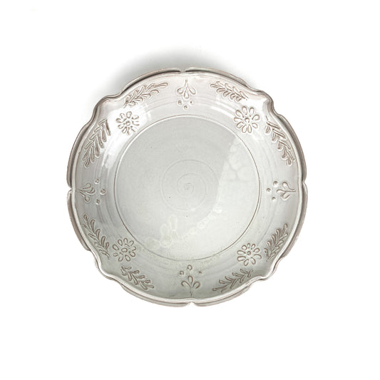 Overhead view of a glazed ceramic plate with a scalloped edge and embossed floral and leaf decorations.