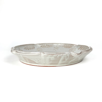 Side view of a shallow, glazed ceramic dish with a scalloped rim and embossed floral and leaf decorations.
