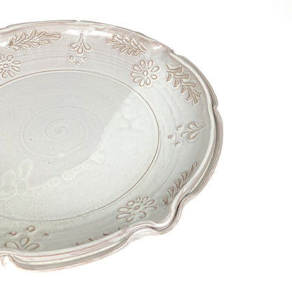 Close-up of a glazed ceramic plate with a scalloped edge and embossed floral and leaf details.