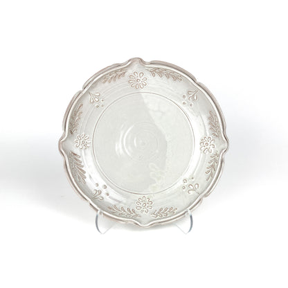 Glazed ceramic plate with a scalloped edge and embossed floral and leaf decorations, displayed on clear stands.