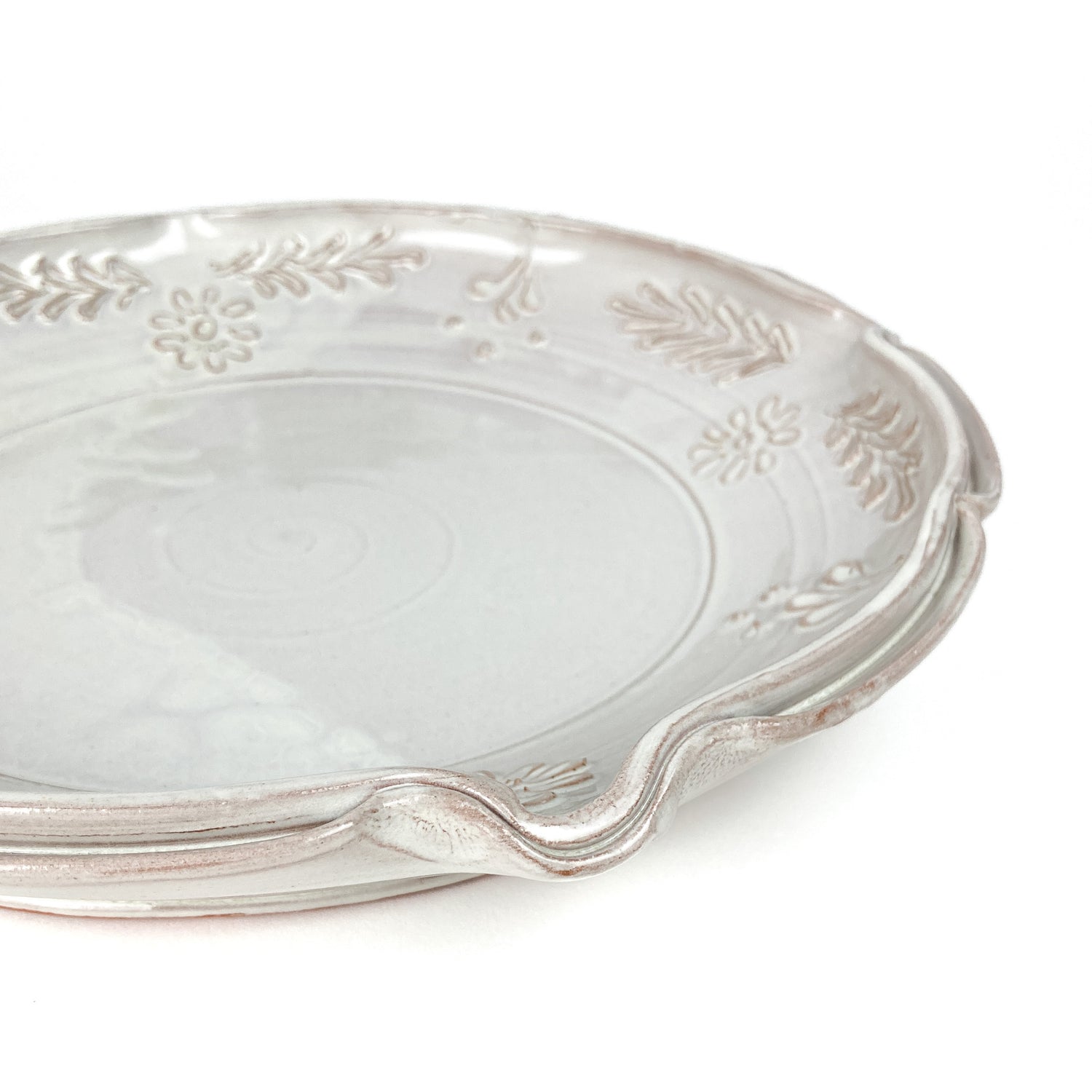 Angled close-up of a glazed ceramic plate with a scalloped edge and embossed floral and leaf details.