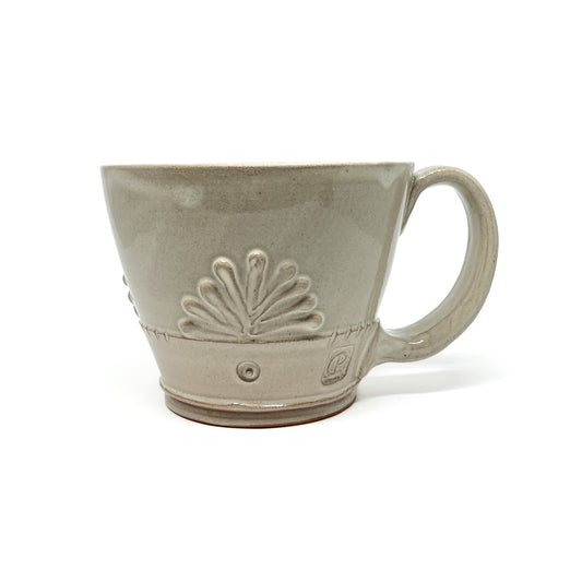 Speckled, glazed ceramic latte mug with an embossed, stylized floral design and a maker's mark.