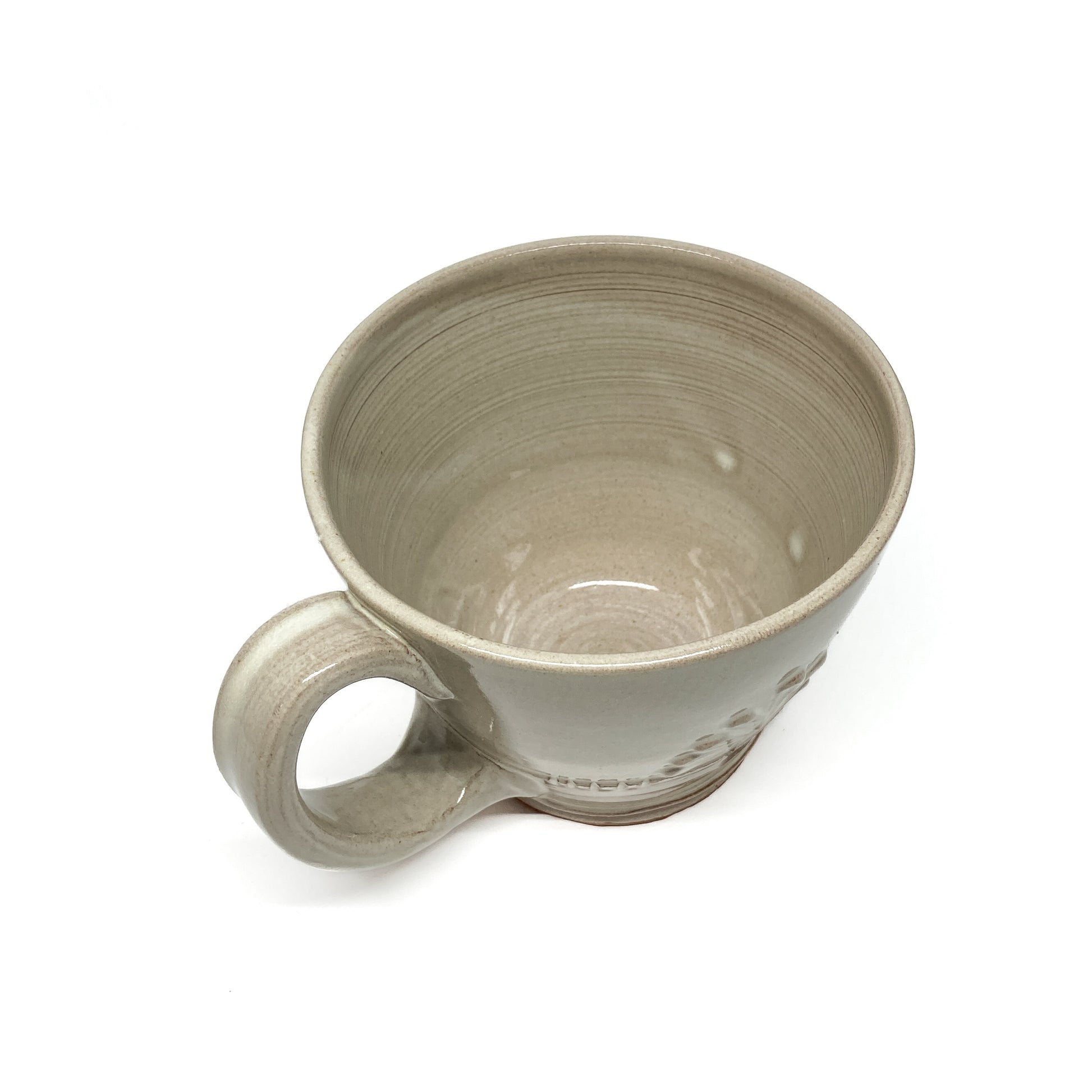 Overhead view of a speckled, glazed ceramic latte mug with an embossed, stylized floral design and a handle.