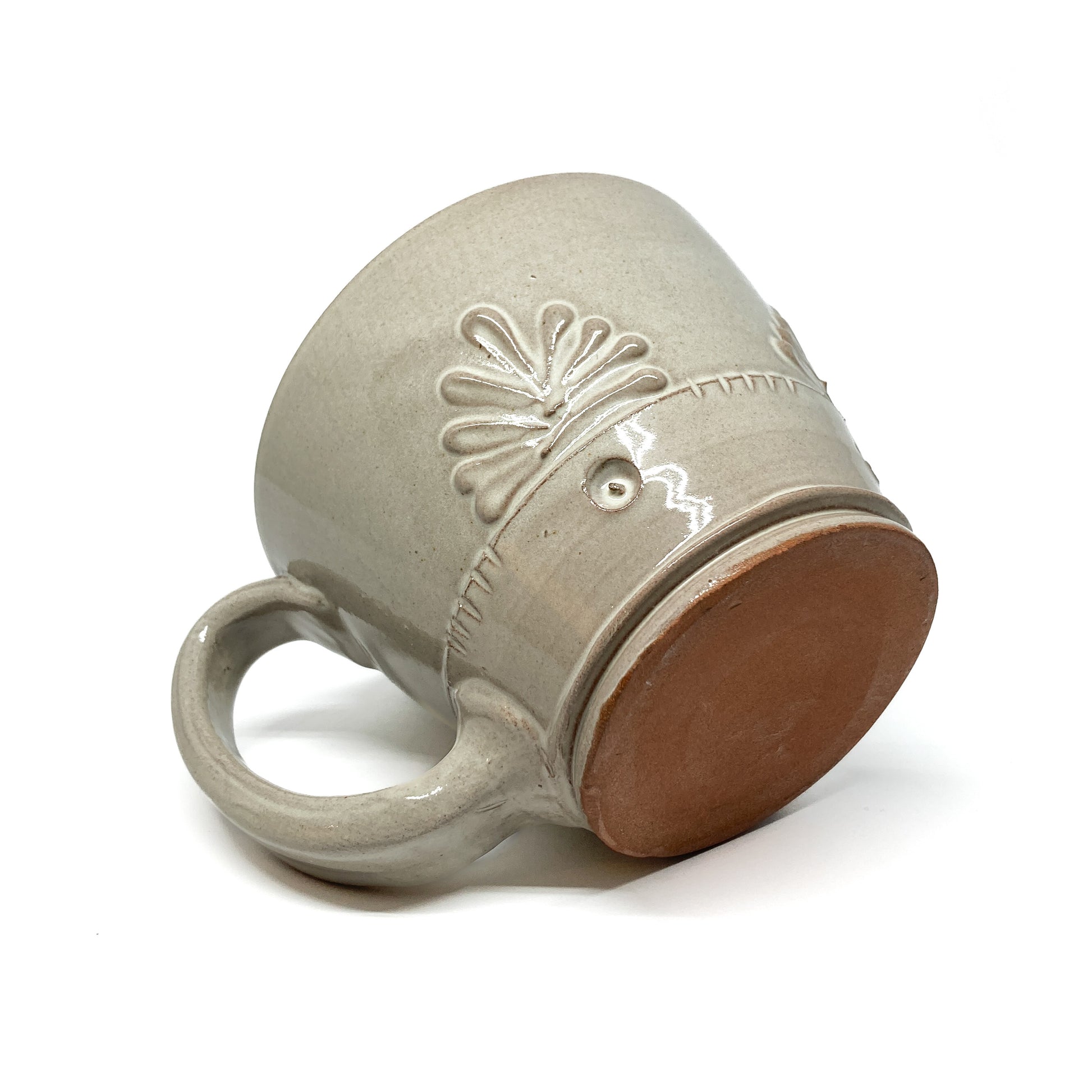 Angled view of a speckled, glazed ceramic latte mug showing the unglazed base and embossed floral design.