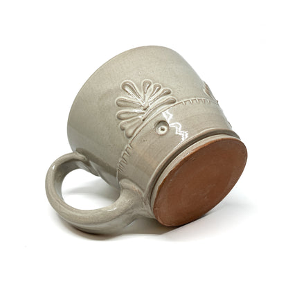 Angled view of a speckled, glazed ceramic latte mug showing the unglazed base and embossed floral design.