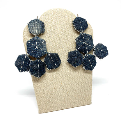 "Patched Chandelier" earrings displayed on a stand. The denim hexagons feature white stitching details.