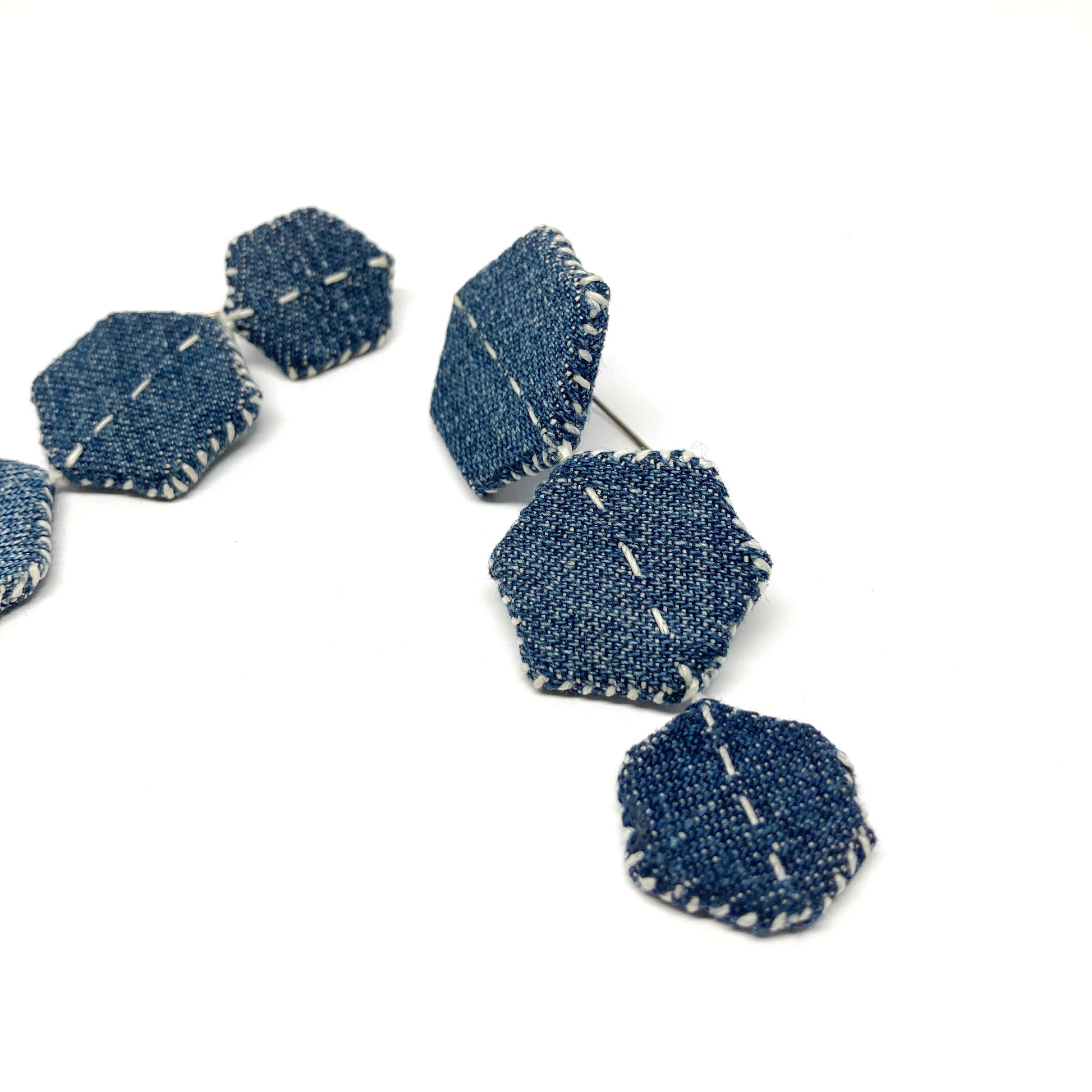 Close-up of one "Patched Trio" earring by Louise Perrone, showing three denim hexagons with white stitching and a post.