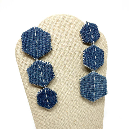"Patched Trio" earrings by Louise Perrone displayed on a textured stand. Each earring features three denim hexagons with white stitching.