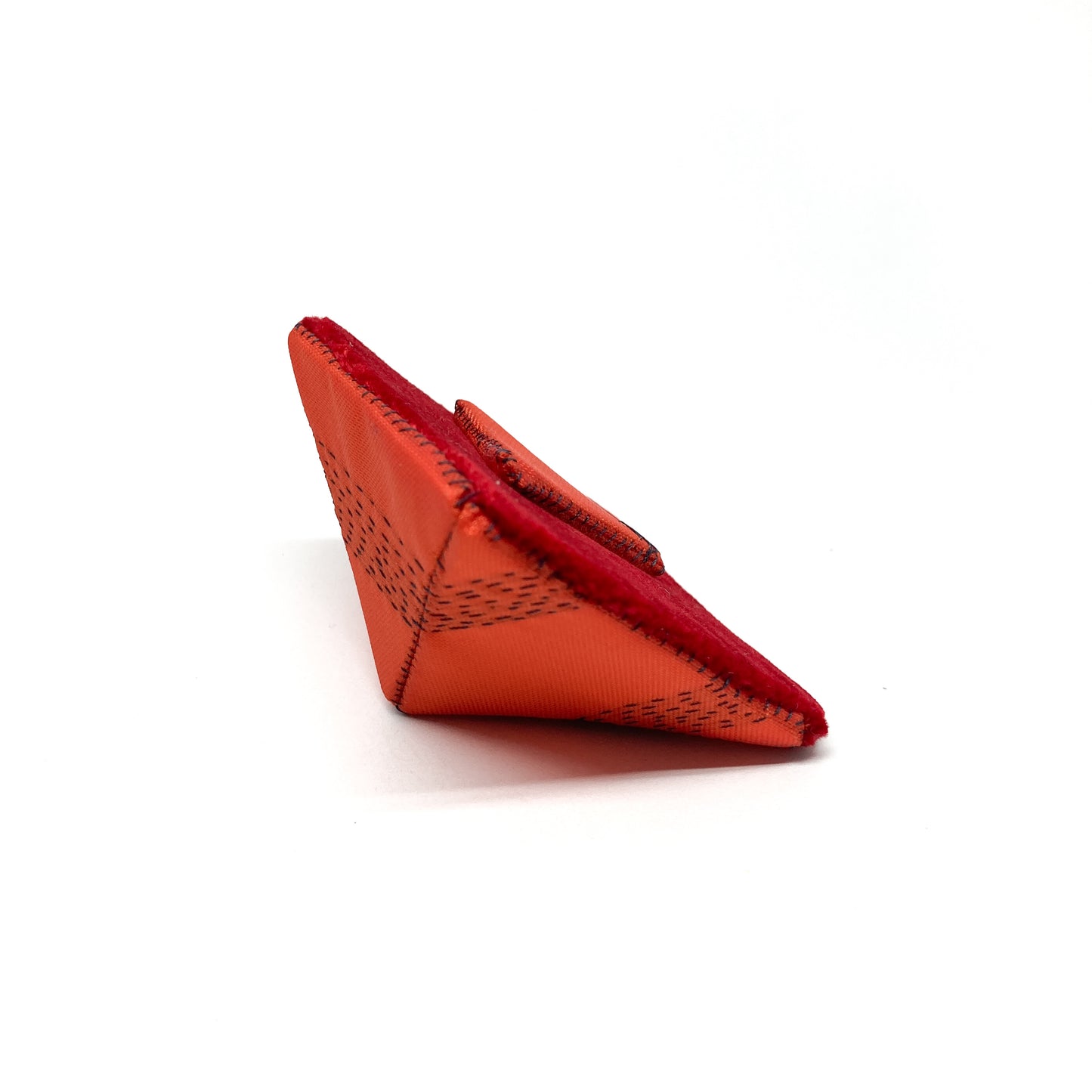 Side view of an orange "Flagged Elevensies" brooch showing its layered form and textured material.