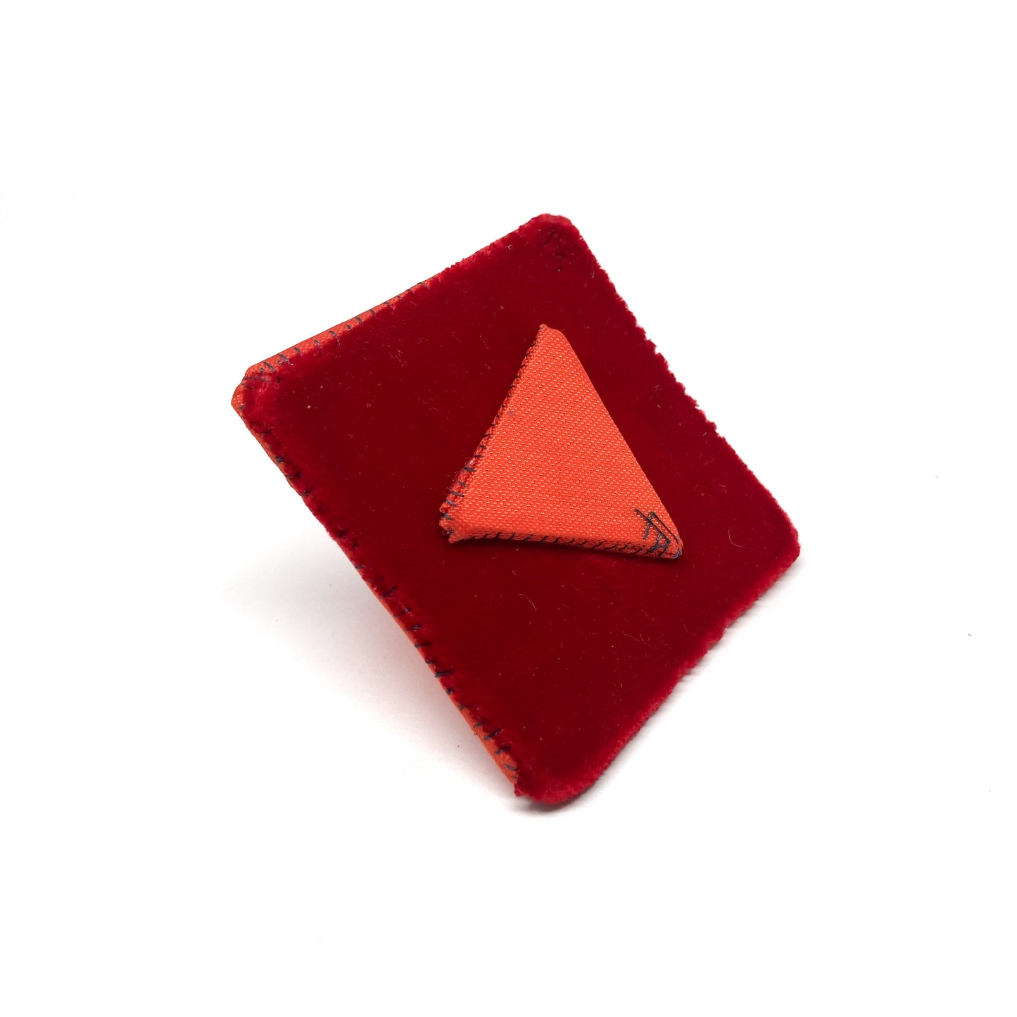 Back of an orange "Flagged Elevensies" brooch with a triangular pin on a square backing.