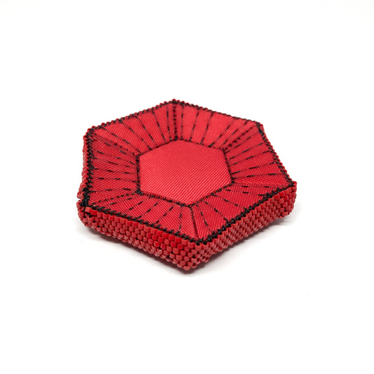 A close-up shows a red, beaded Flagged Obsessions Brooch with black accents, angled slightly to the left.