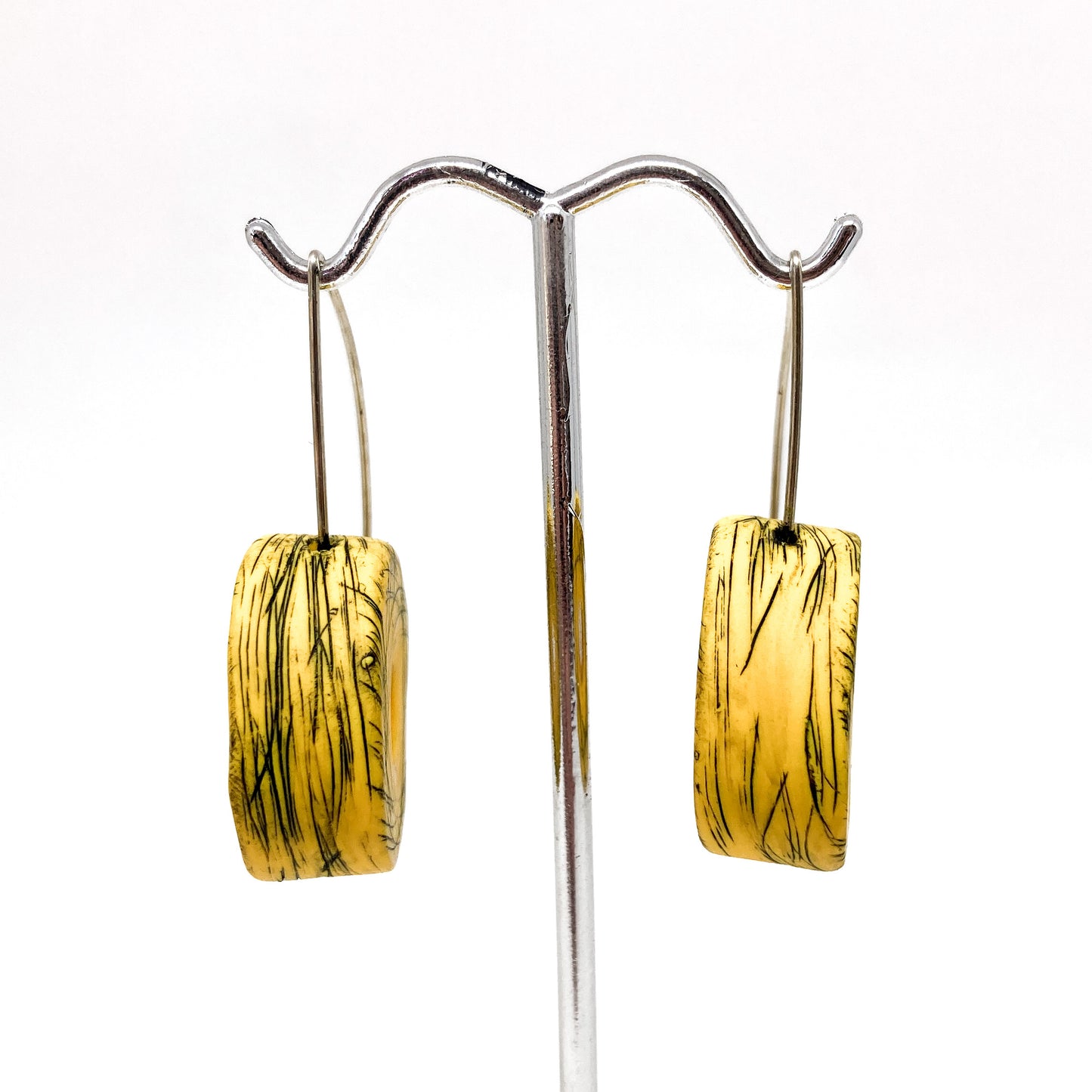Two yellow and green striped rectangular earrings hang from a silver display stand.