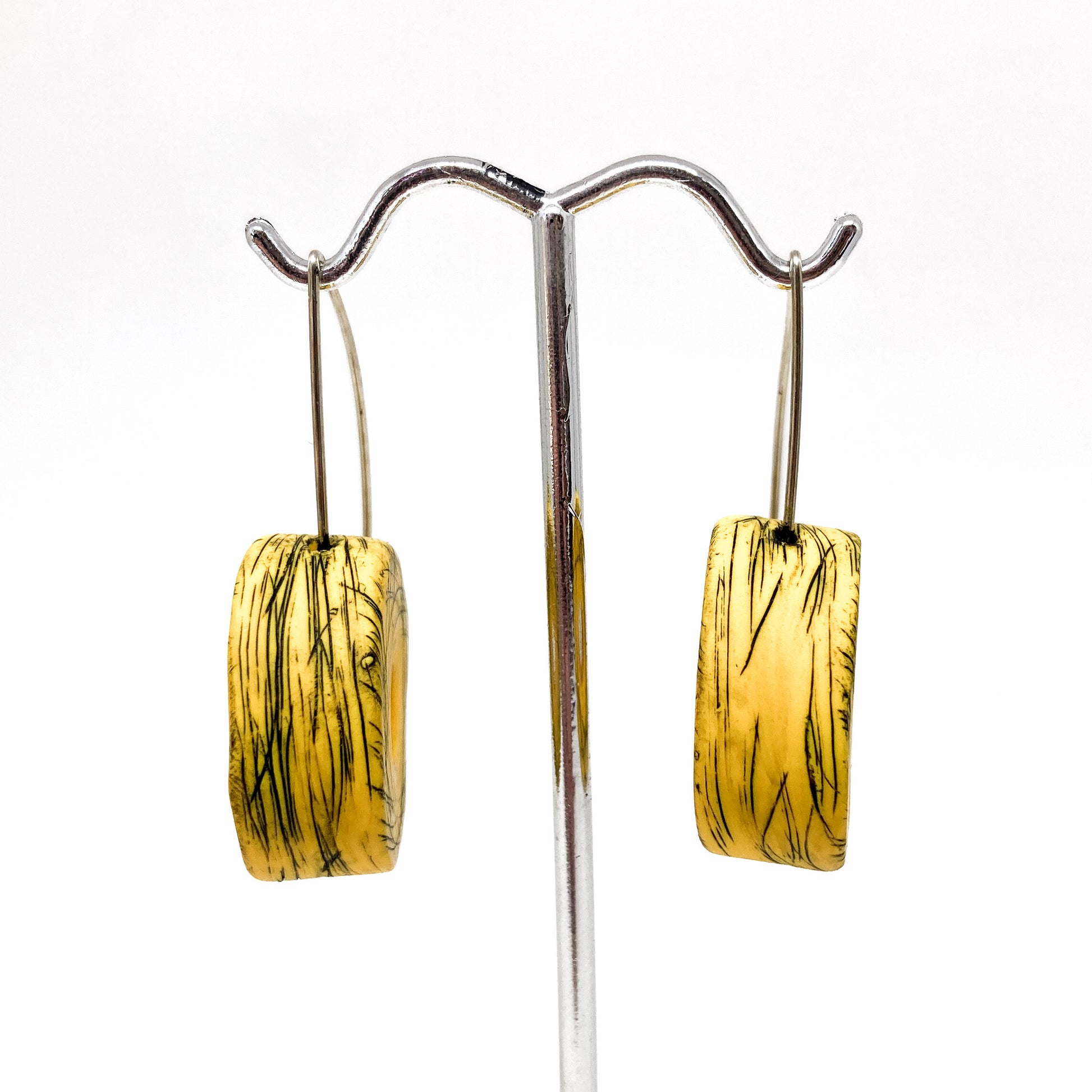 Two yellow and green striped rectangular earrings hang from a silver display stand.