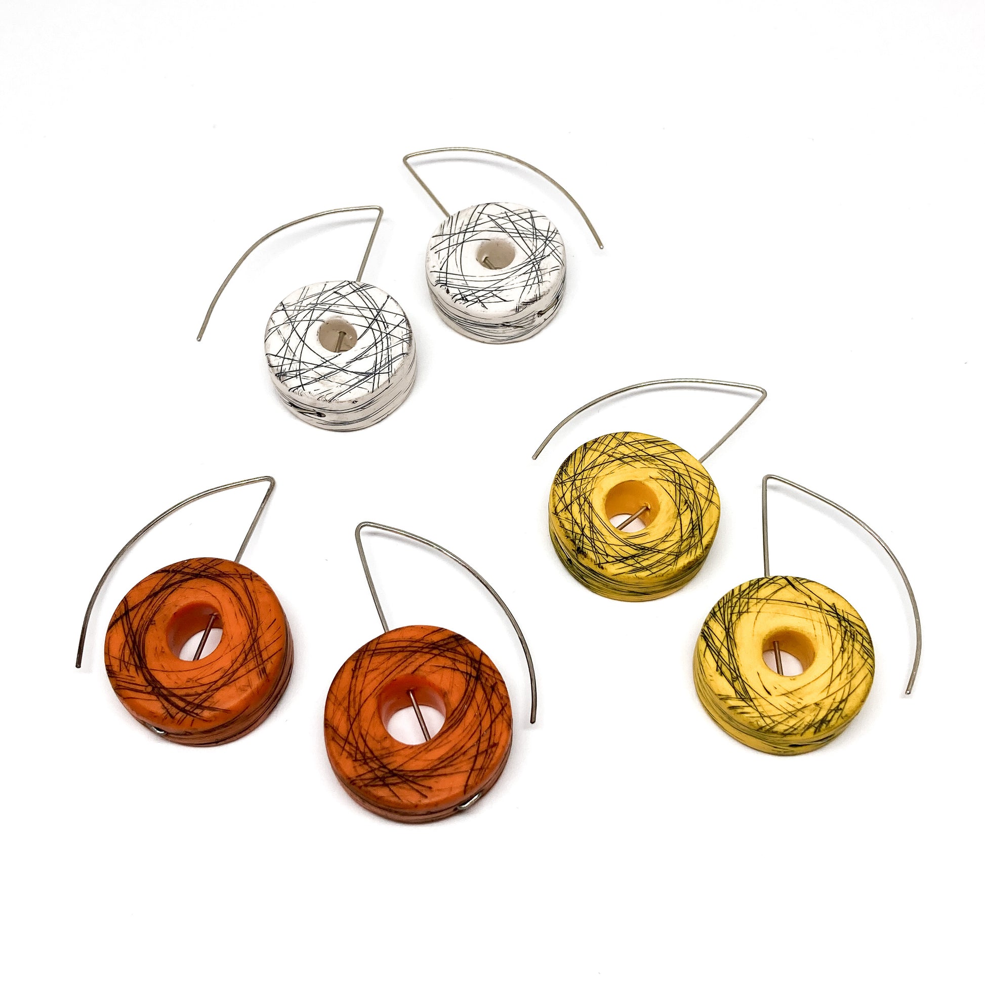 Five striped donut-shaped earrings in white, orange, and yellow hang from silver wires.