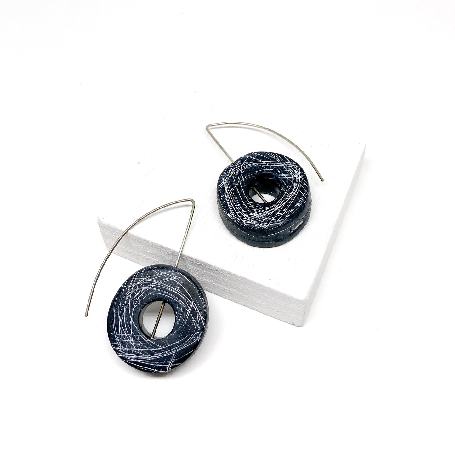 Two black, donut-shaped earrings with white scribbled lines hang from silver hooks.