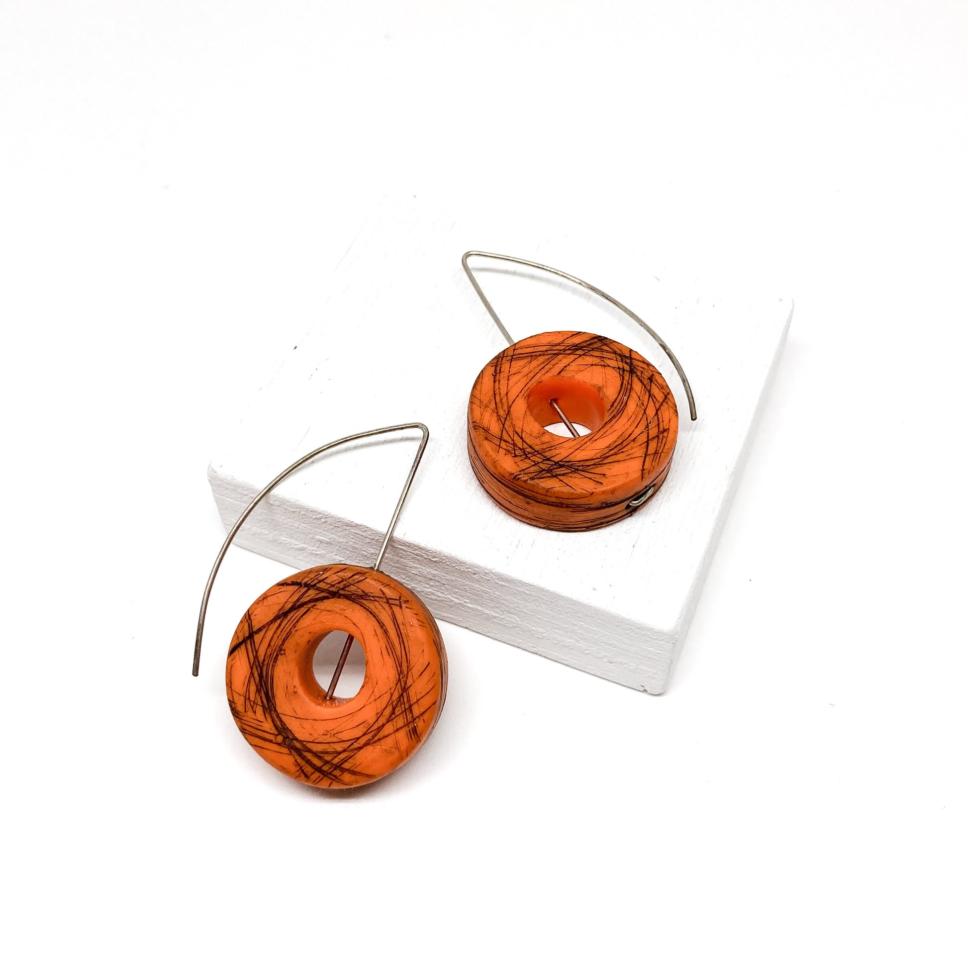 Two orange, donut-shaped earrings with black scribbled lines hang from silver hooks.