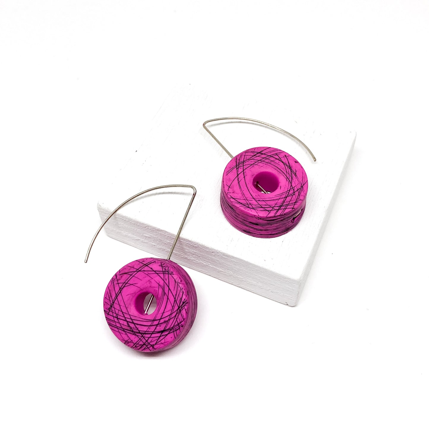 Two magenta, donut-shaped earrings with black scribbled lines hang from silver hooks.