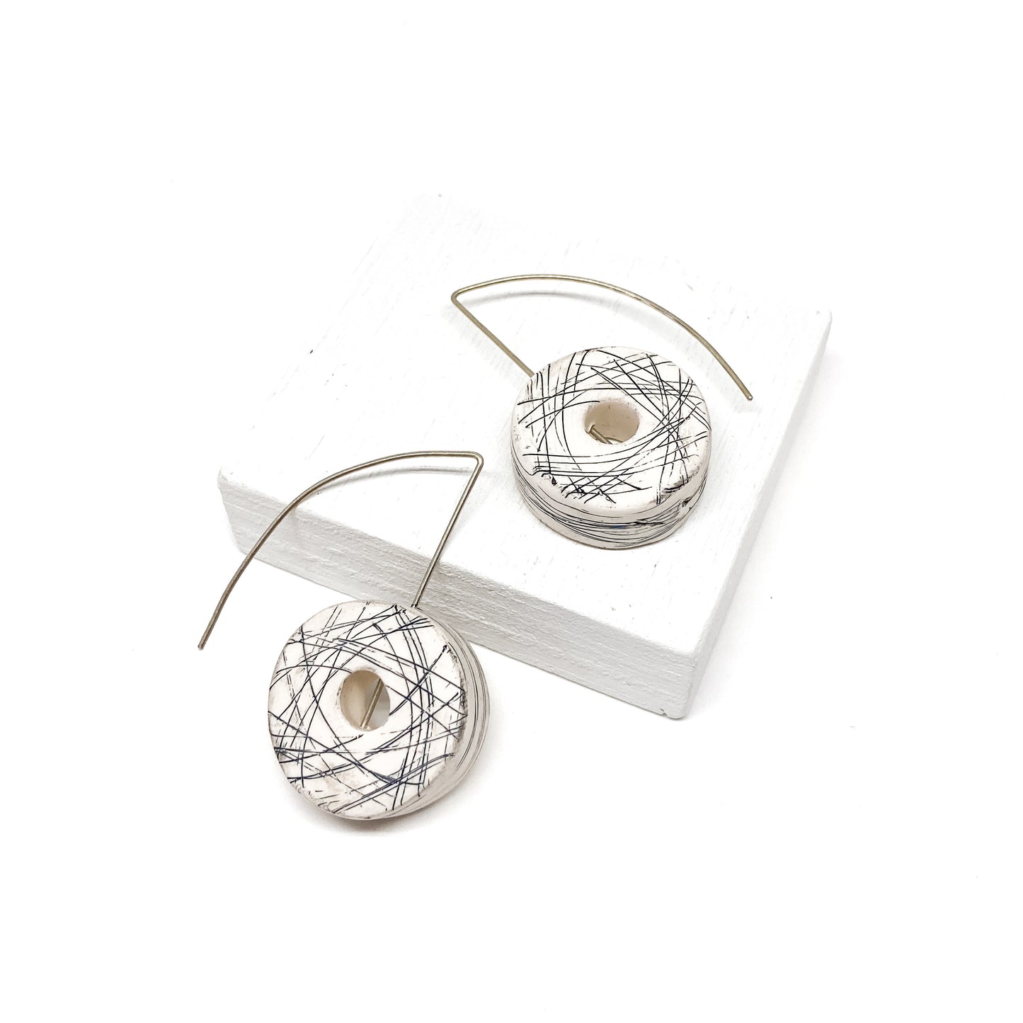 Two white, donut-shaped earrings with black scribbled lines hang from silver hooks.