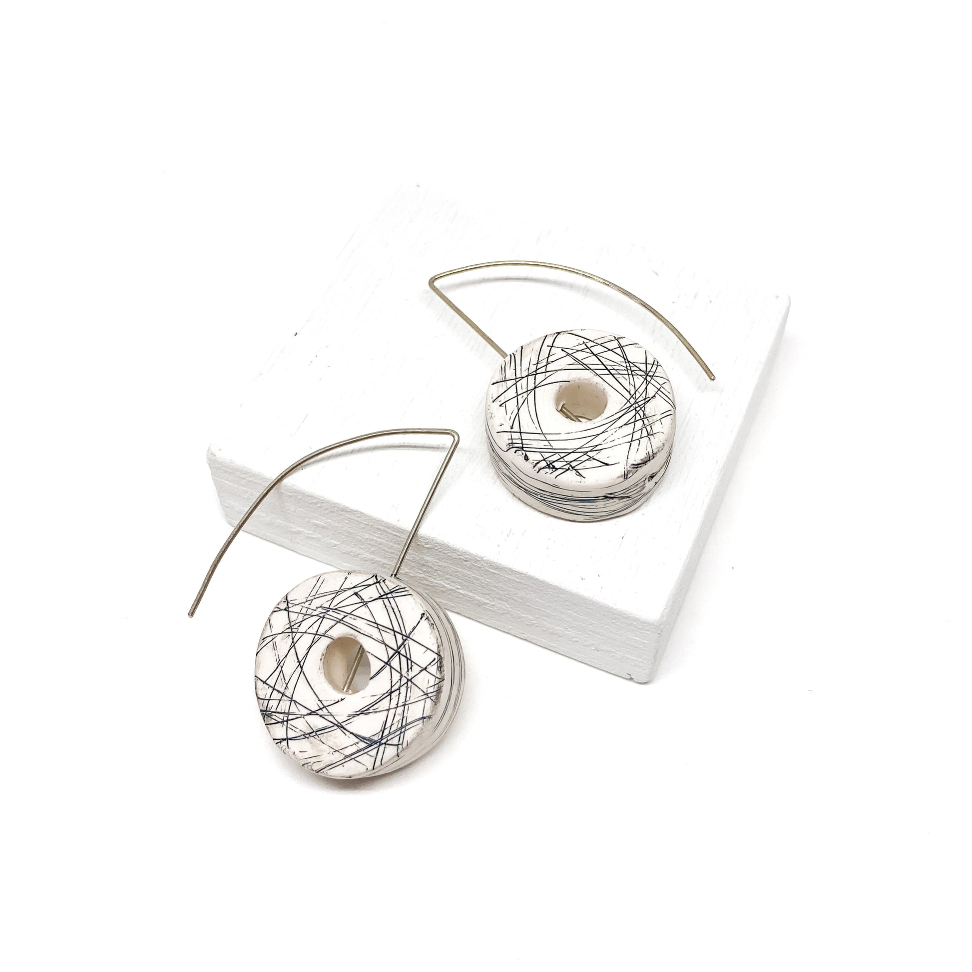Two white, donut-shaped earrings with black scribbled lines hang from silver hooks.