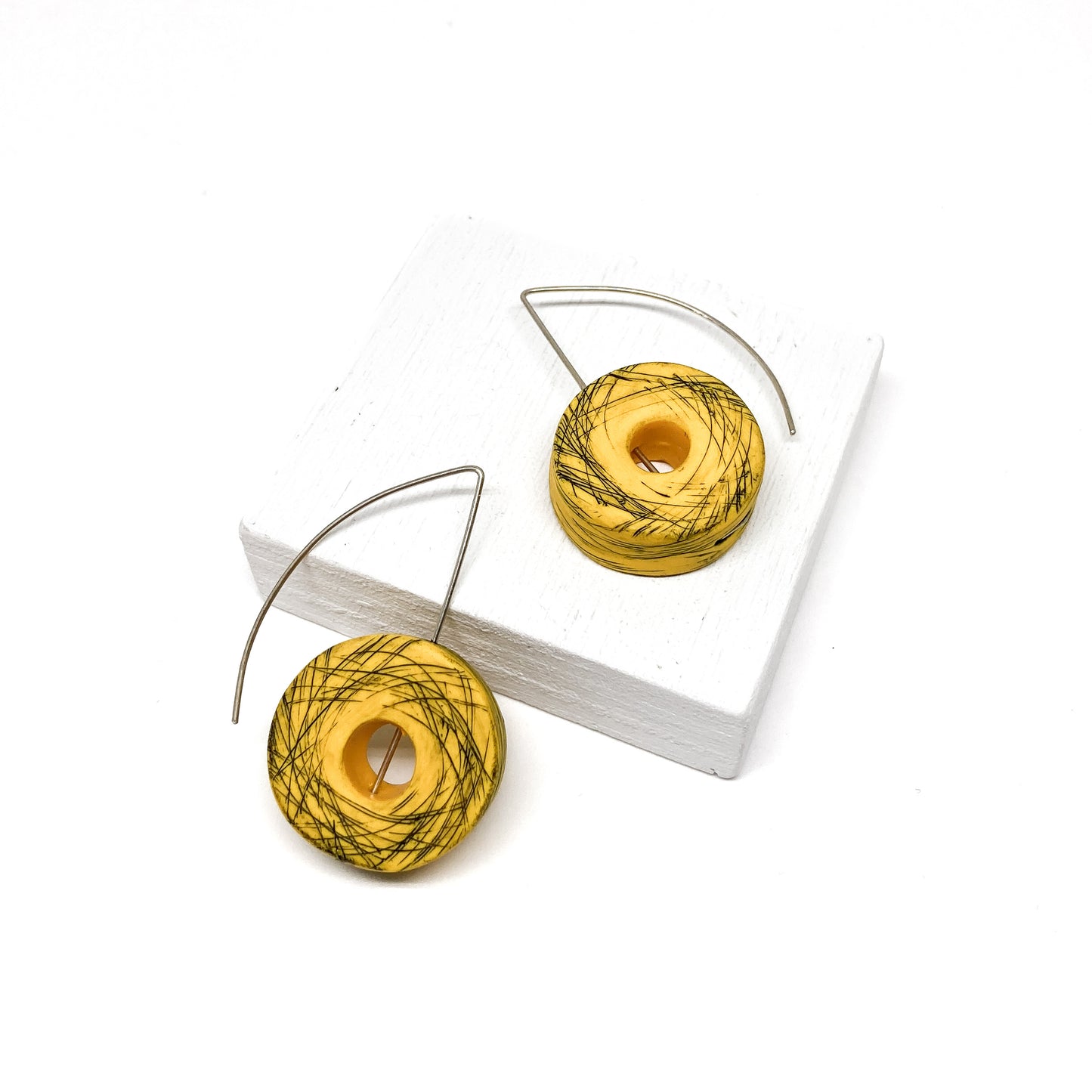 Two yellow, donut-shaped earrings with black scribbled lines hang from silver hooks.