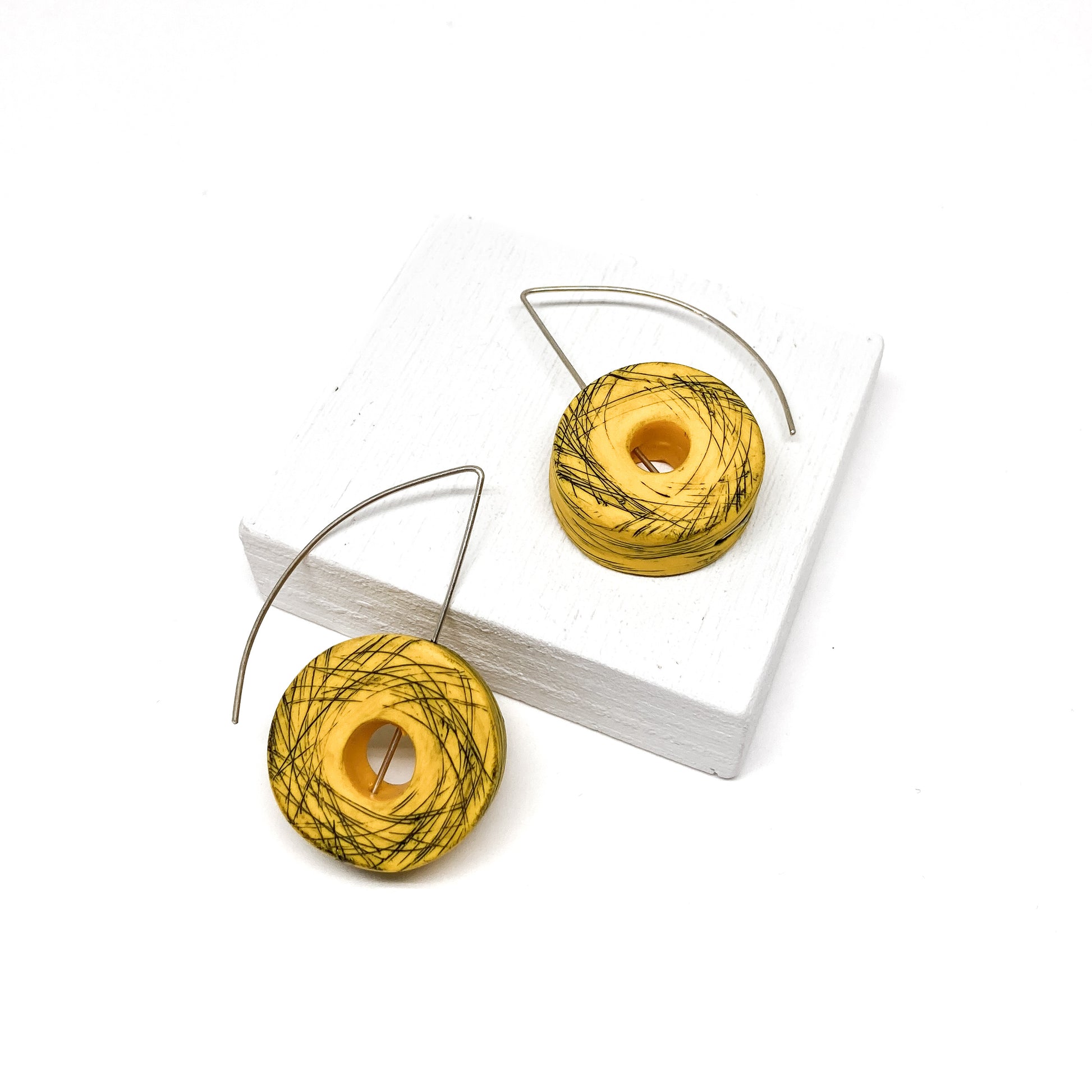 Two yellow, donut-shaped earrings with black scribbled lines hang from silver hooks.