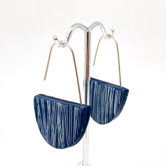Two dark blue, half-circle earrings with white scribbled lines hang from silver hooks.