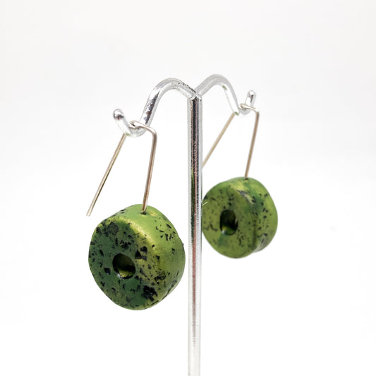 Two green donut-shaped earrings with black speckles hang from silver hooks.
