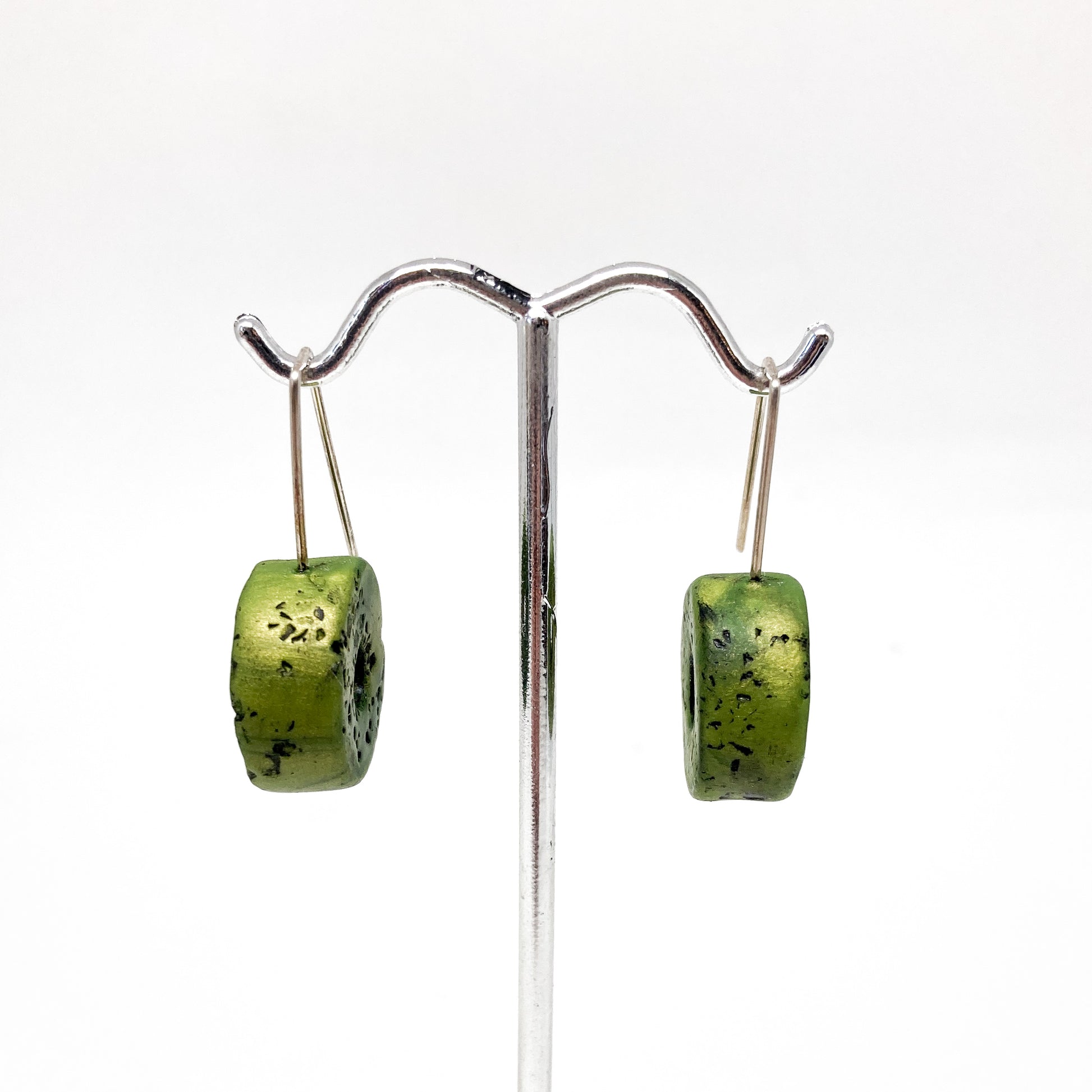 Two green, donut-shaped earrings with black speckles hang from silver hooks.