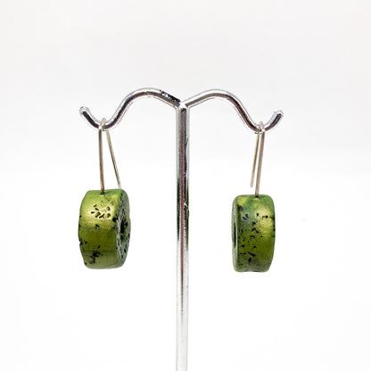 Two green, donut-shaped earrings with black speckles hang from silver hooks.