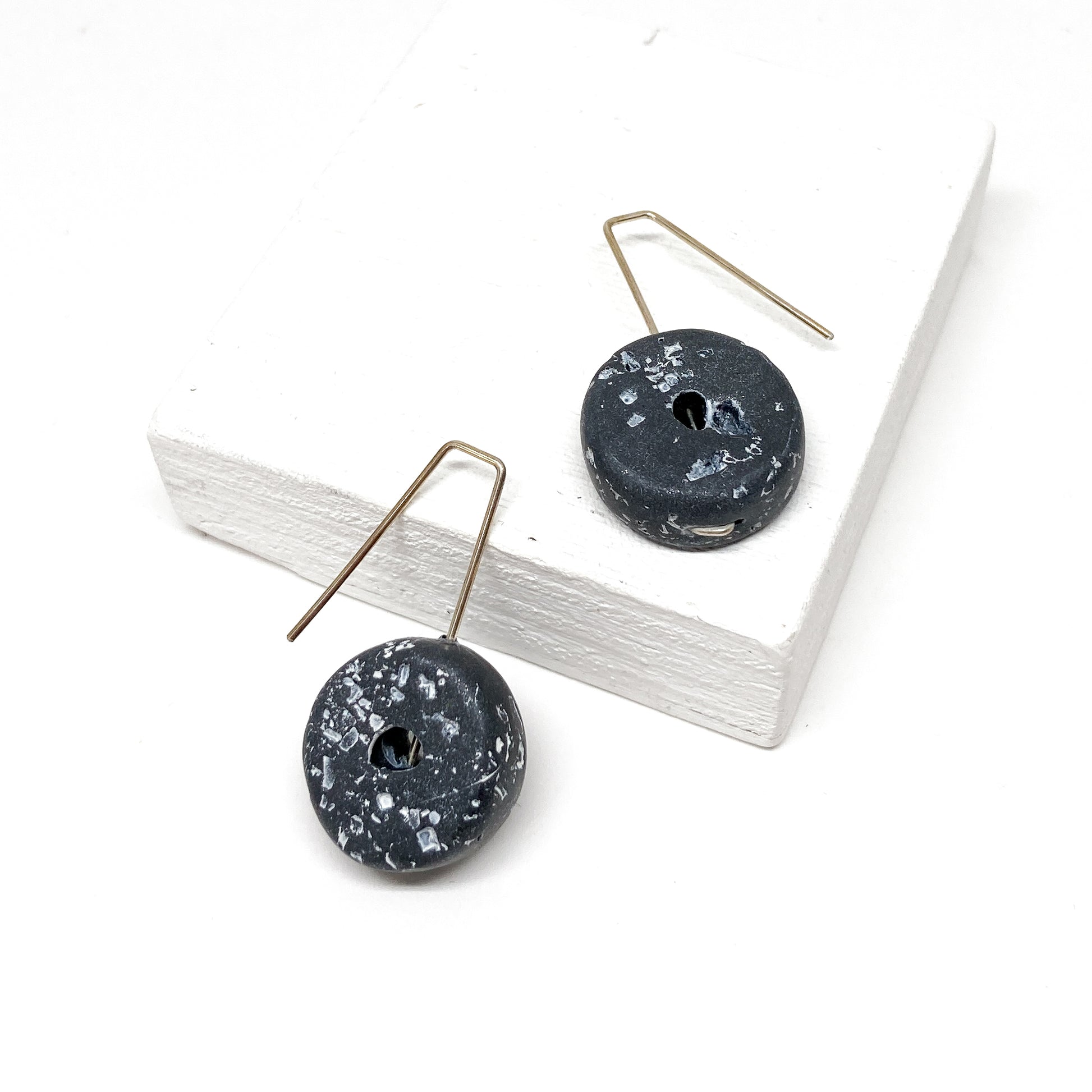 Two black, donut-shaped earrings with white speckles hang from silver hooks.