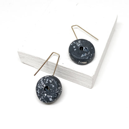 Two black, donut-shaped earrings with white speckles hang from silver hooks.