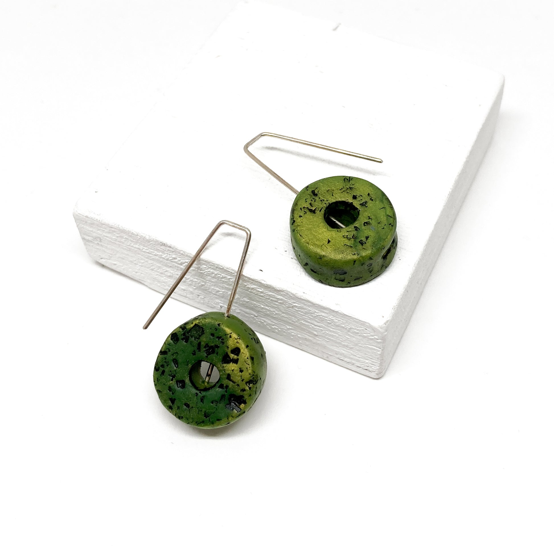 Two green, donut-shaped earrings with black speckles hang from silver hooks.