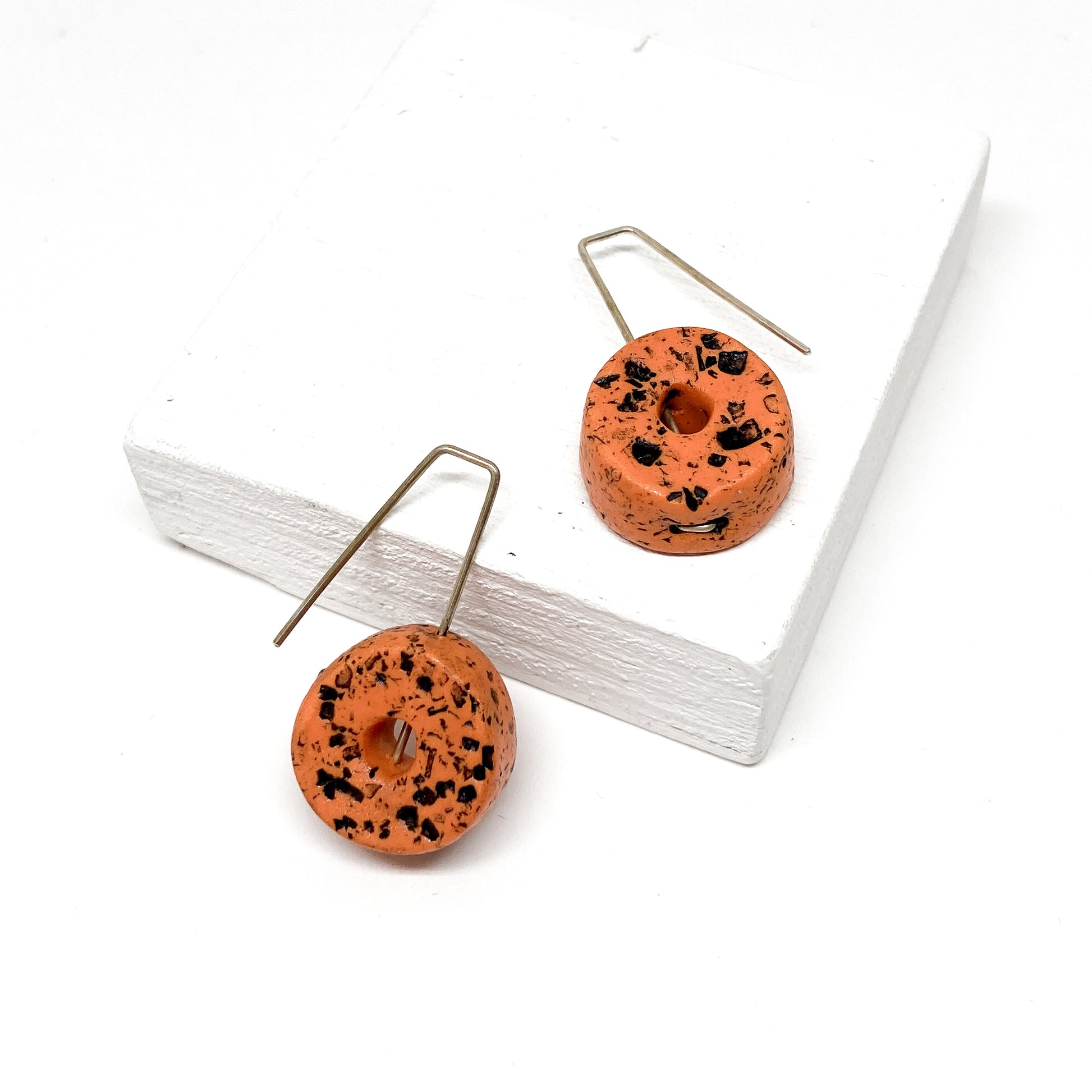 Two orange, donut-shaped earrings with black speckles hang from silver hooks.