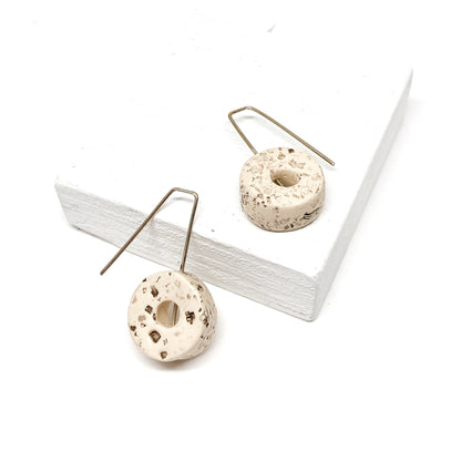 Two white, donut-shaped earrings with brown speckles hang from silver hooks.