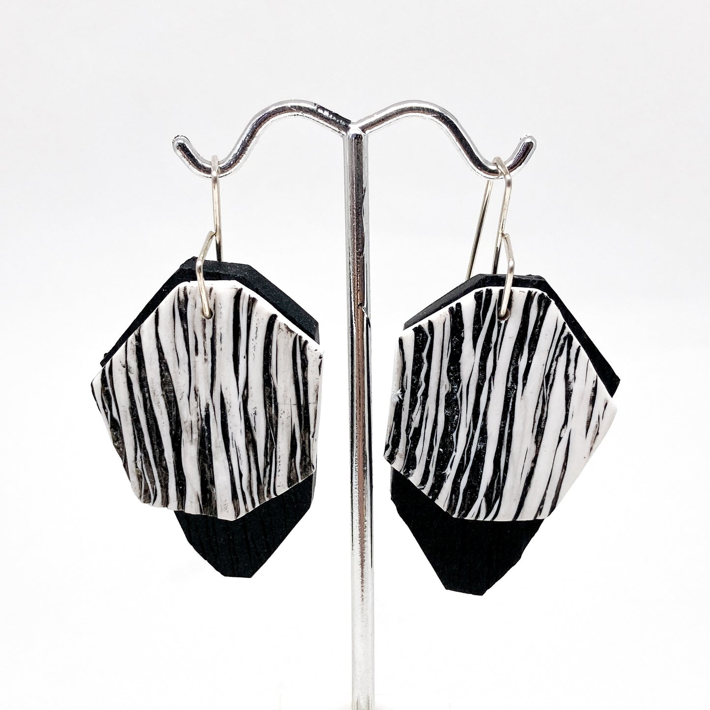 Two black and white, diamond-shaped earrings hang from silver hooks.