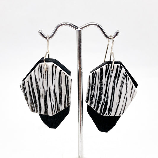 Two black and white, diamond-shaped earrings hang from silver hooks.