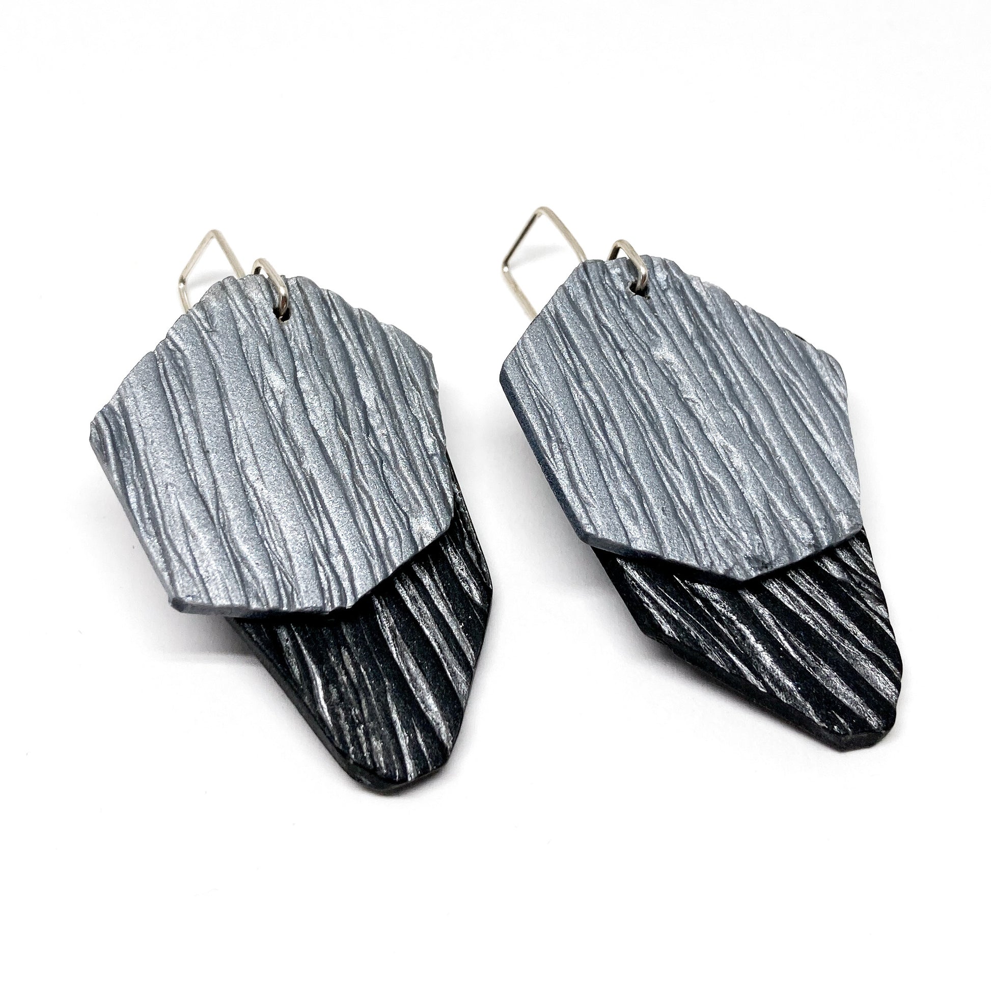 Two textured, silver and black geometric earrings hang from silver hooks.