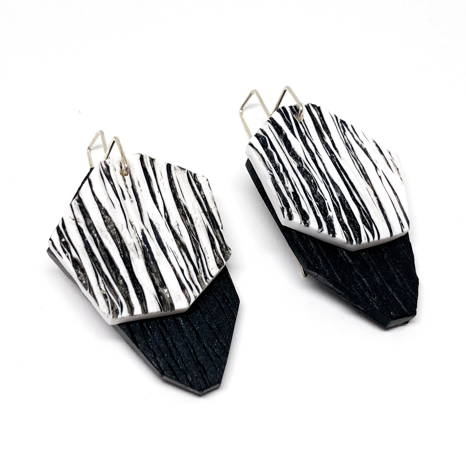 Two textured, black and white geometric earrings hang from silver hooks. They are Cliff Earrings.