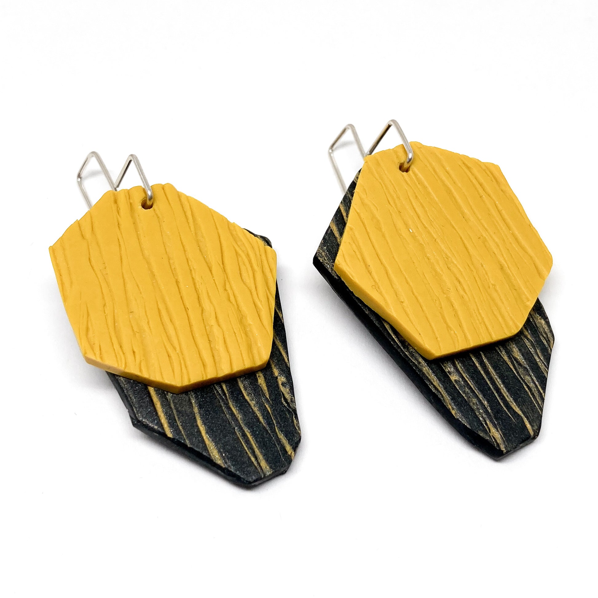 Two textured, yellow and black geometric cliff earrings hang from silver hooks.