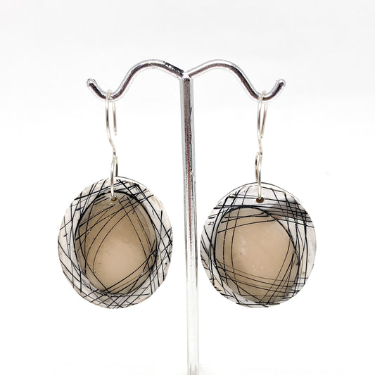 Round handcrafted earrings with abstract black line patterns, hanging on a metal display stand.