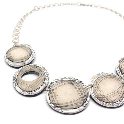 Close-up of a modern necklace with five round pendants featuring abstract black lines, one with a hollow center.