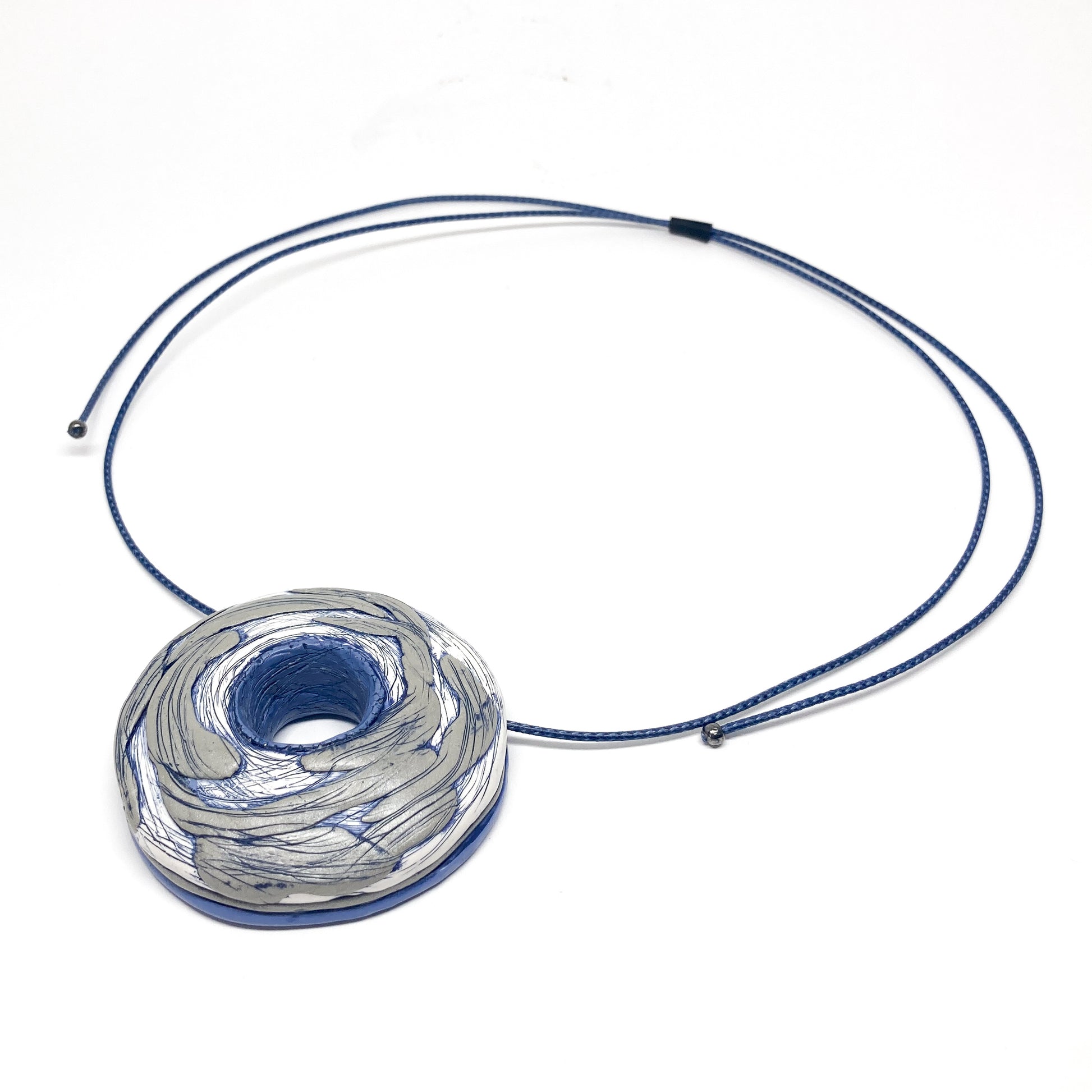 Artistic donut-shaped pendant on an adjustable cord necklace, displayed at an angle.