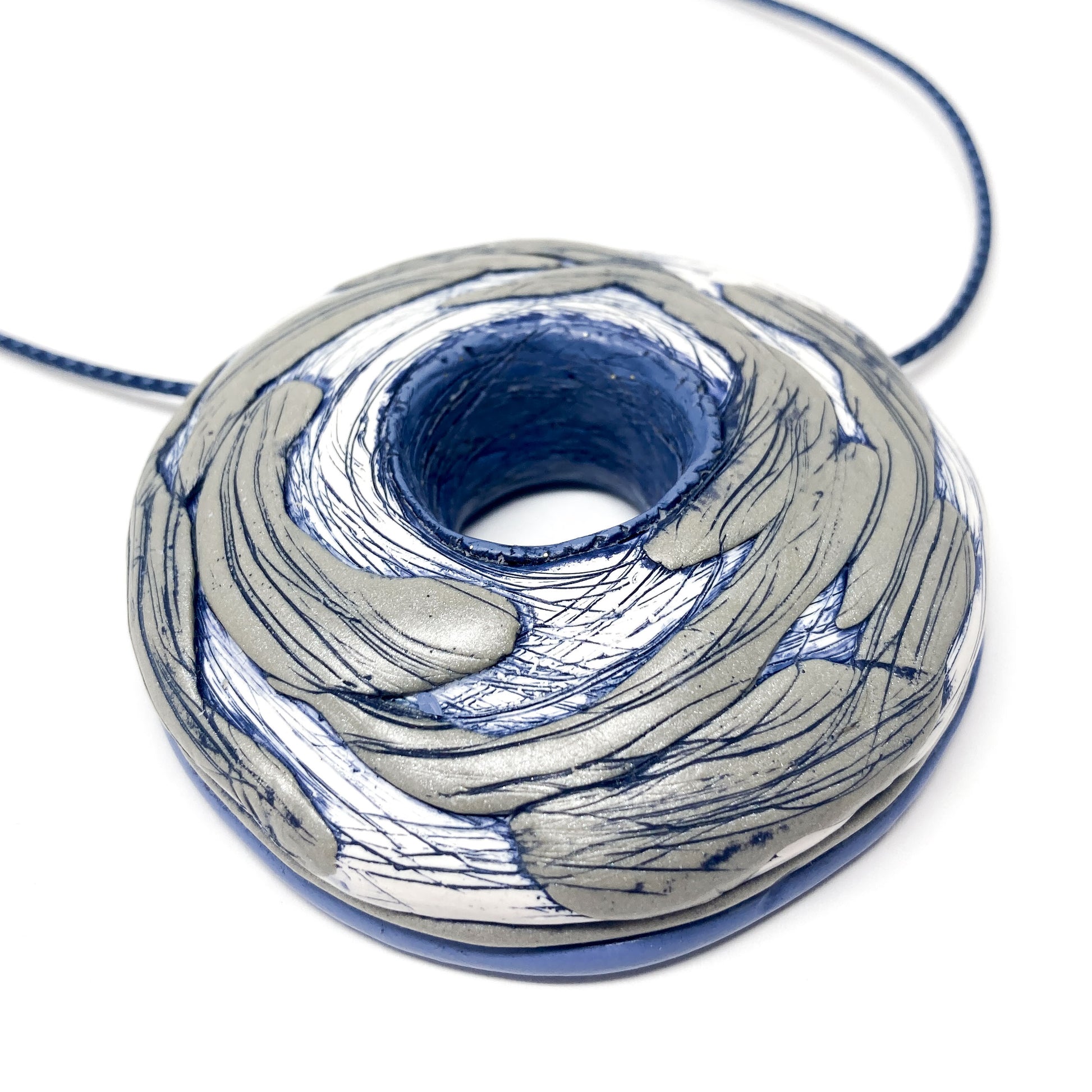 Close-up of a sculptural round pendant with swirling textured surface and central hole on a cord necklace.