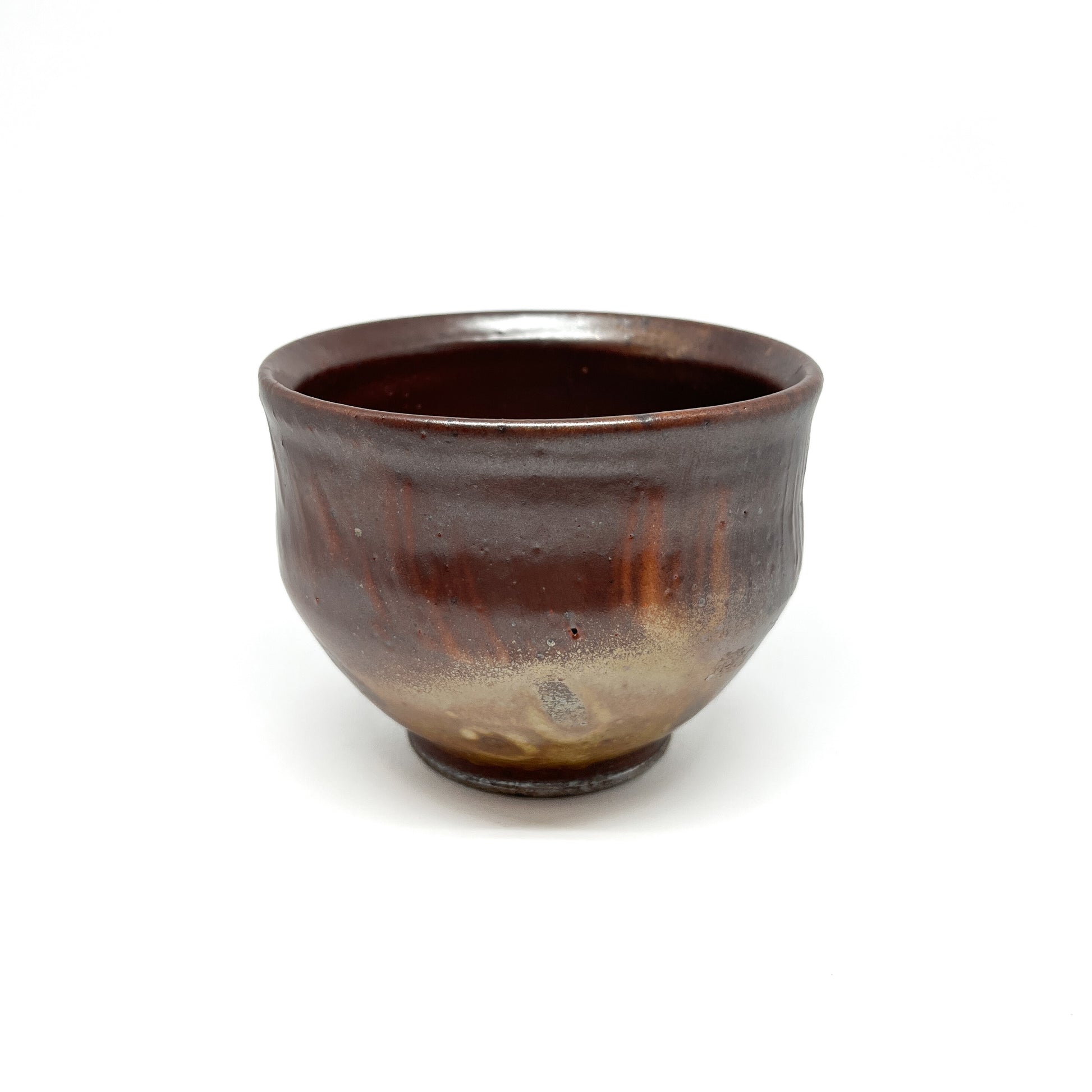 A textured, wood-fired ceramic tea bowl features diagonal markings and variations in tone across its surface.