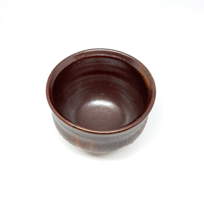 A rustic, dark brown wood-fired tea bowl with subtle variations in texture and glaze.